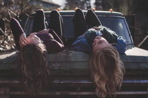 Two people with long hair lying next to each other on the hood of a truck